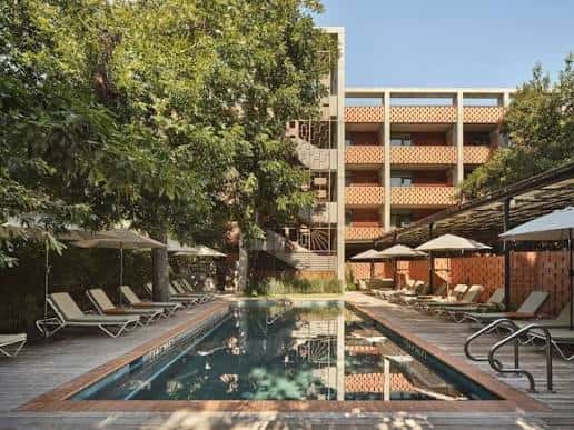 Piscina exterior rodeada de tumbonas y árboles, con fachada de ladrillo del hotel