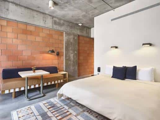 Interior de habitación con cama, mesa de trabajo y pared de ladrillo expuesto