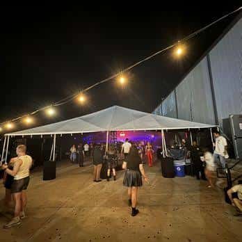Área exterior del The Concourse Project con carpa y luces de cadena para eventos nocturnos