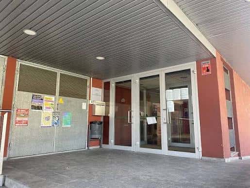 Entrada principal del Local Social con puertas de cristal y cartel informativo