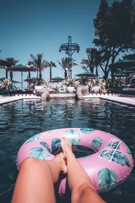 Persona relajándose en la piscina con un flotador rosa