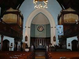 Interior de la iglesia mostrando el altar central, órgano de tubos a ambos lados y vitral circular sobre el altar, ideal para ceremonias o eventos culturales