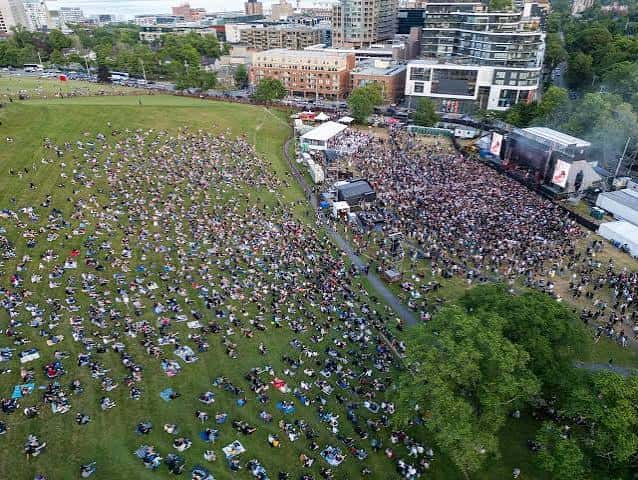 Vista aérea de un evento masivo en Garrison Grounds con público sentado en la hierba