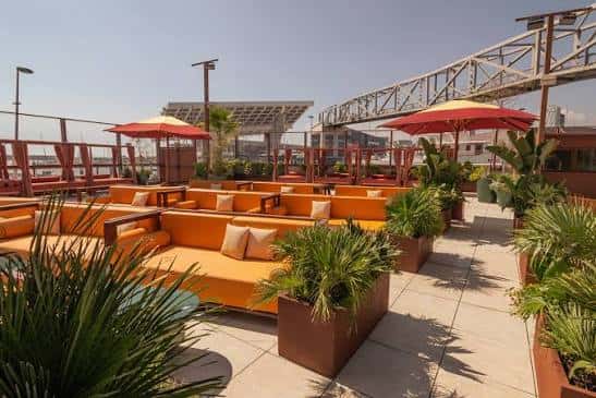 Terraza exterior del club con sofás naranjas, sombrillas y vegetación tropical