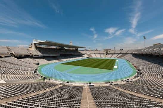 Interior del estadio vacío con pista azul y campo de césped bajo cielo despejado