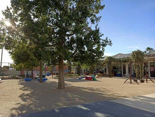 Patio exterior de la escuela con árboles, zona de juegos y edificaciones escolares