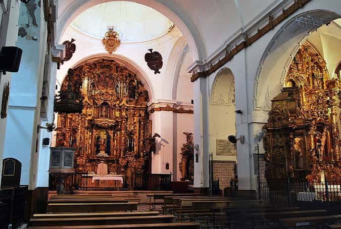 Interior de la iglesia con retablo dorado y bancos de madera bajo luz natural