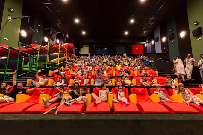Sala de cine familiar con butacas rojas y zona de juegos para niños