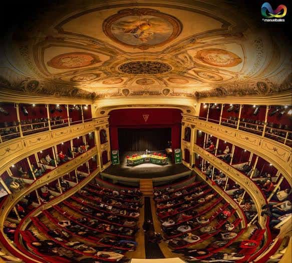 Interior del auditorio con balcones curvos, butacas rojas y techo decorado