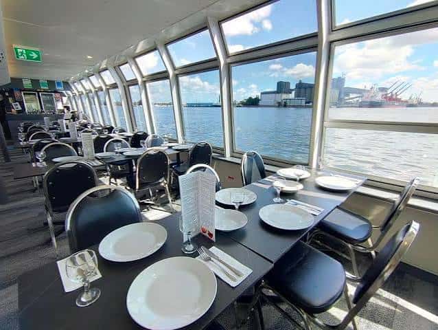 Interior del salón de comedor del crucero con mesas dispuestas para cena y vistas al puerto a través de grandes ventanales