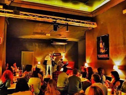 Concierto en vivo con banda en el escenario y público en mesas
