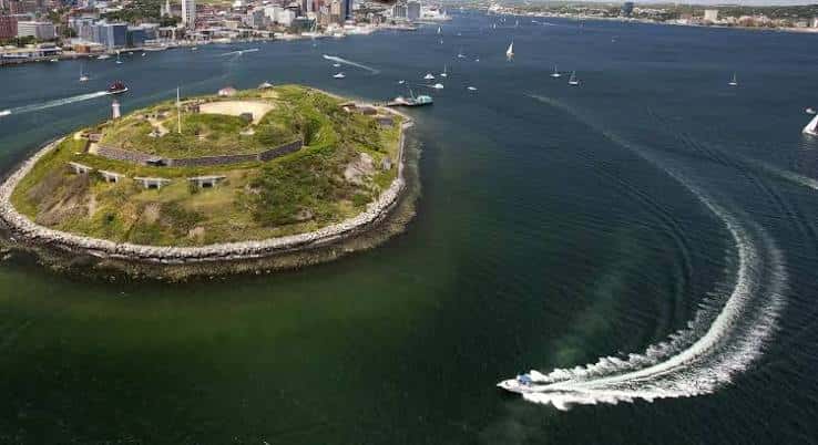 Georges Island rodeada de agua con veleros y un bote a motor en primer plano