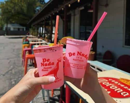 Dos personas brindando con bebidas rosas en la terraza de De Nada Cantina