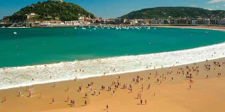 Playa de La Concha con bañistas y veleros en el mar bajo un cielo despejado