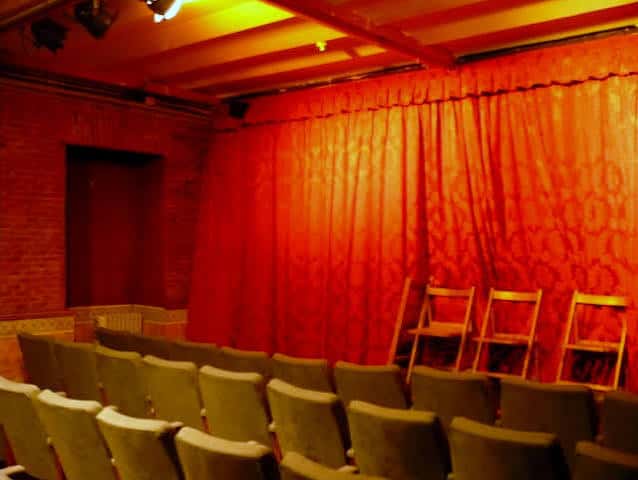 Vista lateral del auditorio del Teatro Karpas con cortinas rojas y butacas grises