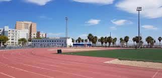 Pista de atletismo al aire libre con césped central y edificios urbanos al fondo