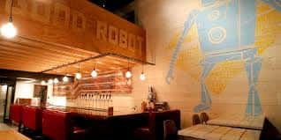 Interior del bar de Good Robot Brewing con barra, luces colgantes y mural de robot