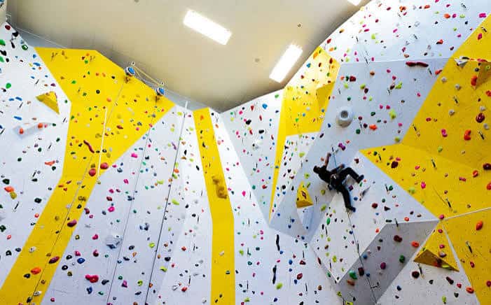 Vista interior de la pared de escalada con secciones amarillas y blancas y múltiples presas de colores
