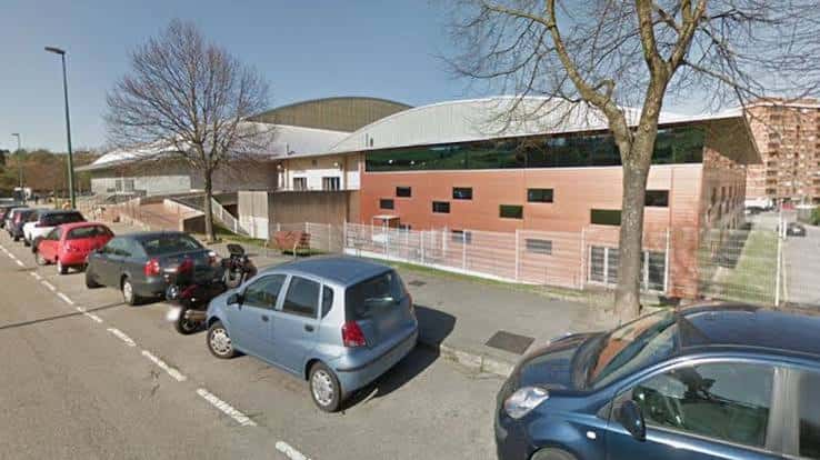 Fachada lateral del complejo deportivo con aparcamiento y árboles