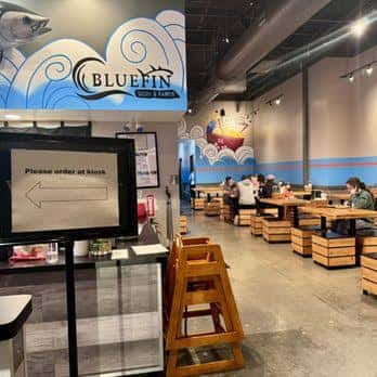 Interior del restaurante con mesas de madera, iluminación moderna y murales artísticos en las paredes