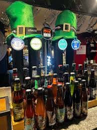Barra con grifos de cerveza decorados con sombreros verdes y botellas de bebidas