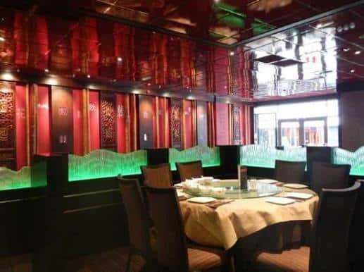 Mesa redonda con mantel beige en el interior del restaurante, rodeada de sillas y con fondo de paneles rojos decorados