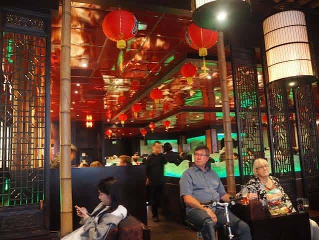 Vista del interior del restaurante con lámparas rojas colgantes, techos reflectantes y comensales sentados