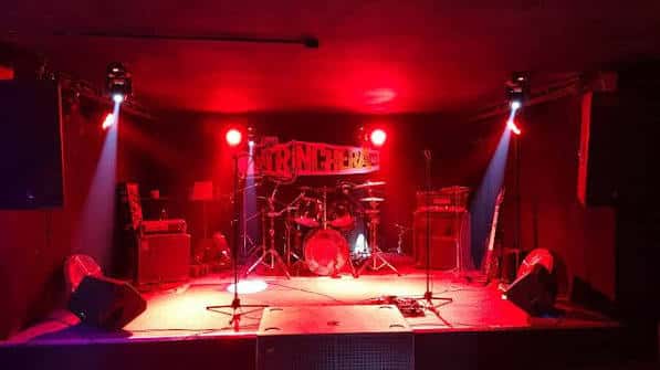 Escenario de la sala La Trinchera iluminado con luces rojas y equipo musical listo para un concierto