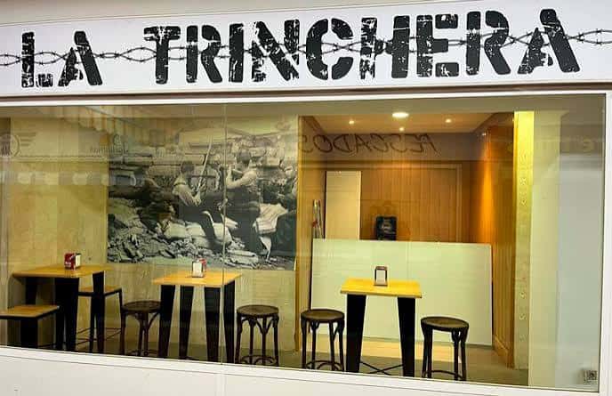 Interior del local La Trinchera con mesas altas y decoración temática de guerra