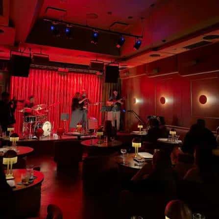 Sala de eventos con escenario y banda en vivo, ambiente íntimo