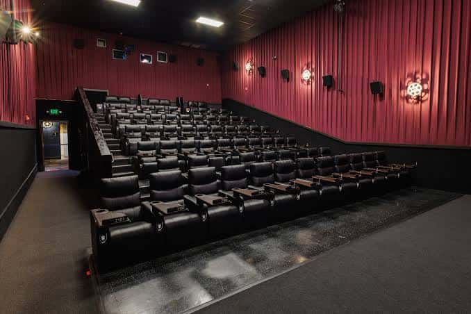 Interior del cine con butacas reclinables negras y paredes rojas, ideal para eventos de cine en vivo