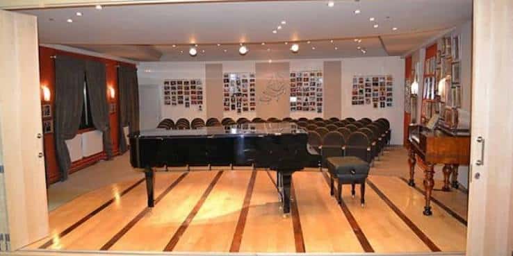 Vista desde la entrada de la Sala Eutherpe mostrando el escenario con piano y disposición del auditorio