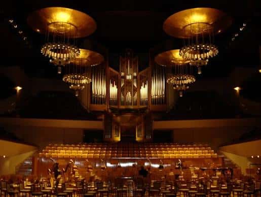 Vista interior del auditorio con iluminación cálida, destacando el gran órgano y las lámparas colgantes doradas