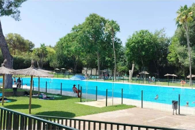 Vista panorámica de la piscina municipal con césped y sombrillas