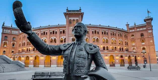 Estatua de un torero frente a la fachada iluminada de Las Ventas al atardecer