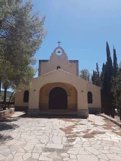 Fachada de la ermita bajo cielo azul con árboles circundantes