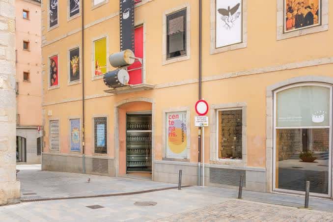 Vista diurna de la fachada del Museu del Cinema con carteles y señalización en la calle
