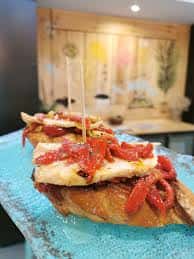 Plato de pinchos con pimientos asados y queso sobre base de pan, presentado en plato azul