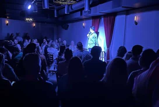 Espectáculo de comedia en vivo con público y comediante en el escenario bajo luces azules