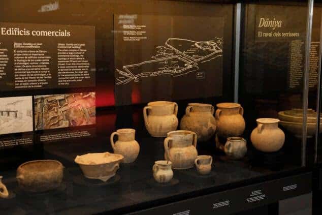 Exposición de cerámicas antiguas en vitrina con mapas históricos