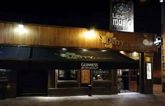 Fachada nocturna de Derry Irish Tavern con iluminación cálida y letrero de 'Live music'