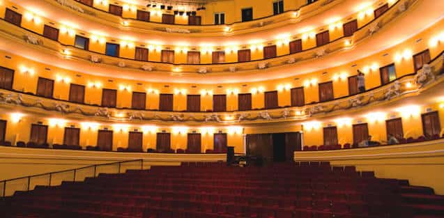 Interior del auditorio con balcones curvos, butacas rojas e iluminación cálida