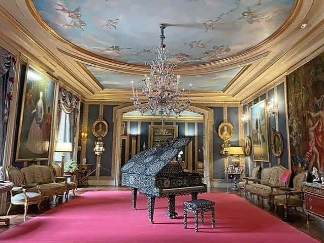 Salón principal con piano decorado, alfombra roja y techo pintado