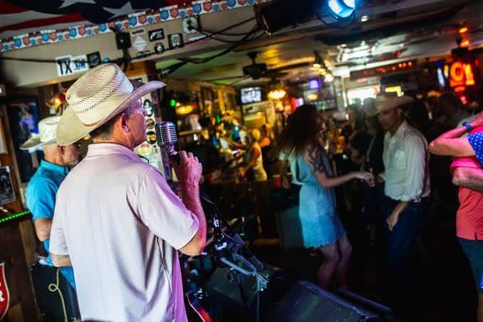 Interior del saloon con clientes bailando y un músico tocando en vivo