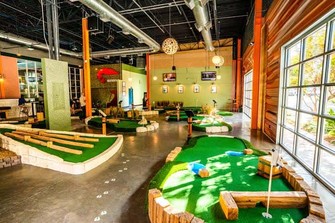 Campo de mini golf interior con obstáculos y grandes ventanales