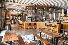 Interior del taproom de Zilker Brewing Company con barra de madera y tanques de fermentación