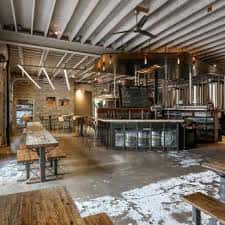Vista panorámica del interior del taproom con mesas de madera y techo industrial