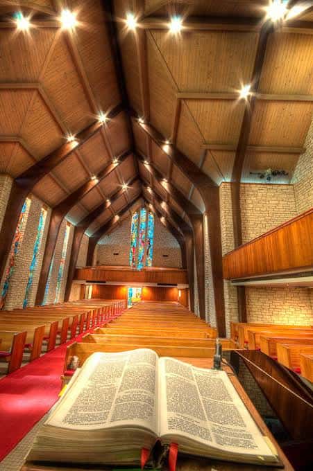 Vista del pasillo central hacia el altar con un libro abierto en primer plano y techo de vigas de madera