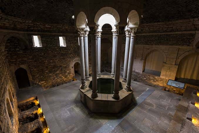 Interior de los Baños Árabes iluminado con luz cálida, mostrando el estanque central y arcos