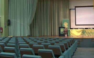 Interior del Paraninfo con cortinas verdes, pantalla de proyección y decoración para evento